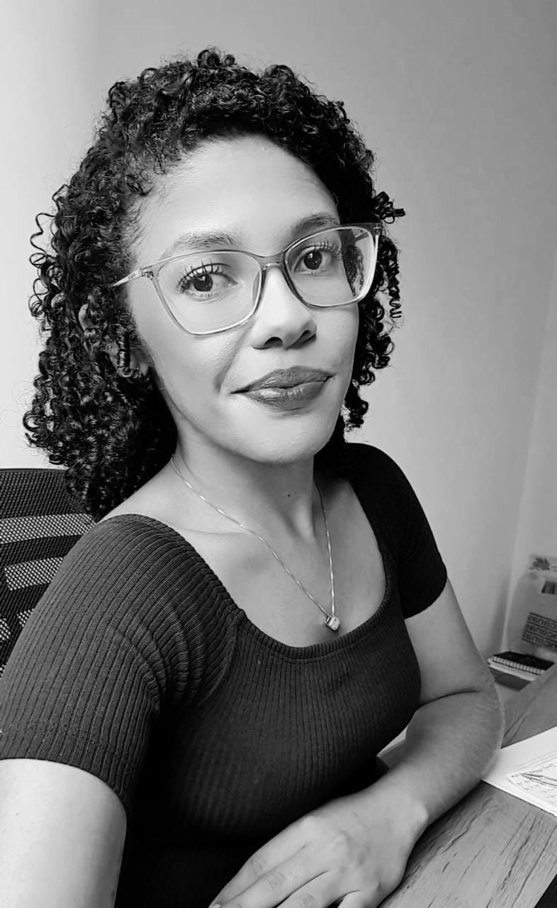 Foto de leticia keller feliz, usando óculos e cabelo cacheado.